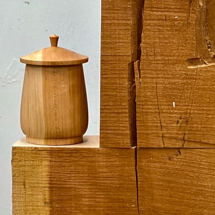 Image of small wooden box turned on a lathe, which is sitting on a block of wood.